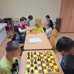 Rozgrywki szachowe. Chłopcy siedzą naprzeciwko siebie przy dwóch stołach i grają w szachy.