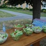 Na stole w parku leżą sałatki warzywne i woda w butelkach.