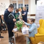 Alicja siedzi w otoczeniu zaproszonych gości, którzy czekają na podpisanie książki.