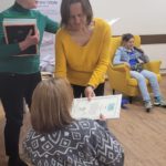Pani Aneta wręcza podziękowanie Oliwii za udział w warsztatach dziennikarskich. Obok siedzi Alicja i stoi pani Agnieszka.
